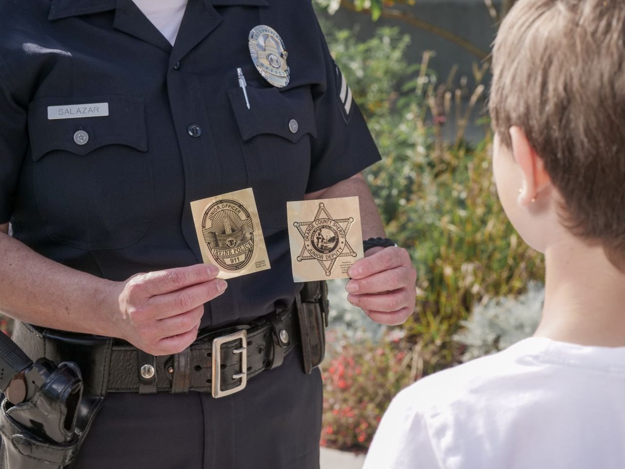 Mastering the First Impression: Your intriguing post title goes here Officer showing law enforcement badges to a child outdoors, fostering positive interaction.